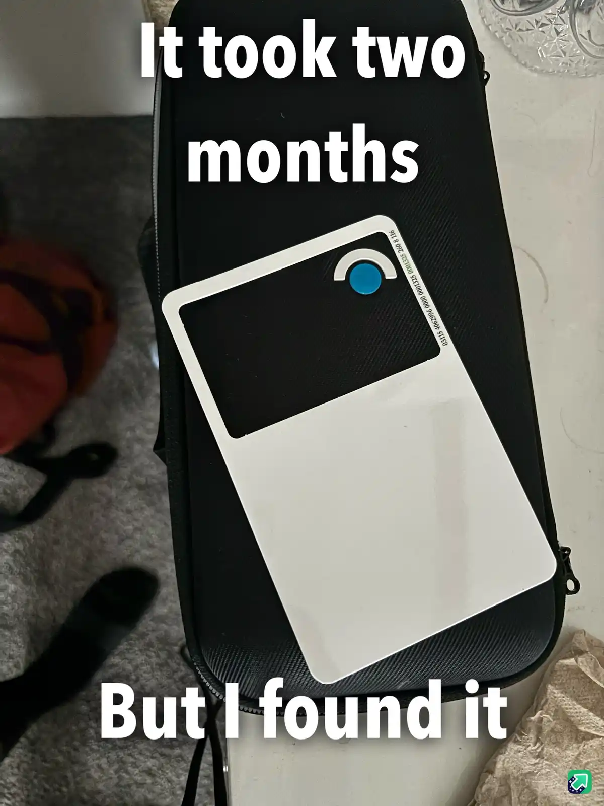 A white and black rectangular device with a blue button sits on a black textured case. Large white text overlaid on the…