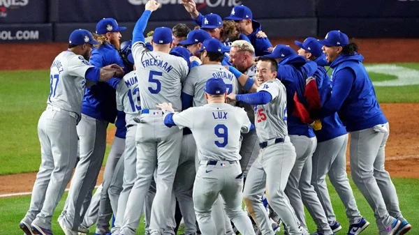 A group of baseball players in Dodgers uniforms are huddled together in celebration on a baseball field. Several players…