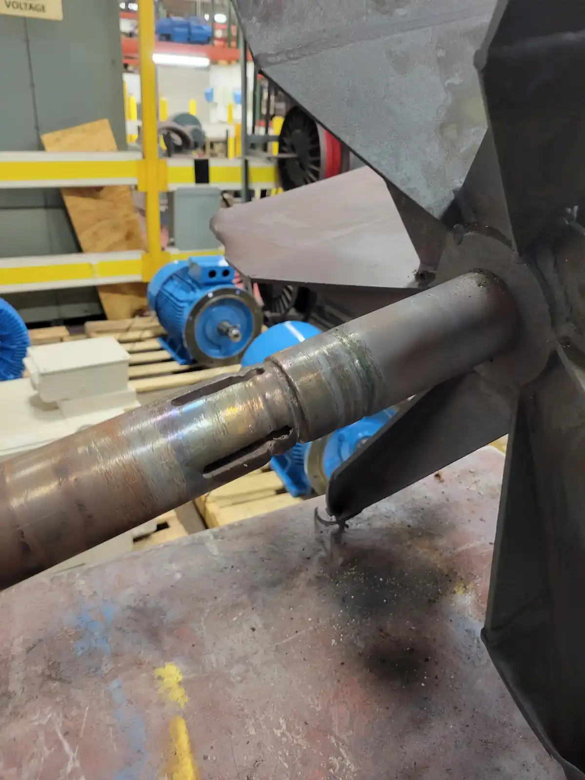 A close-up photo of a rusty, industrial metal shaft with a welded joint, set against a cluttered workshop background with…