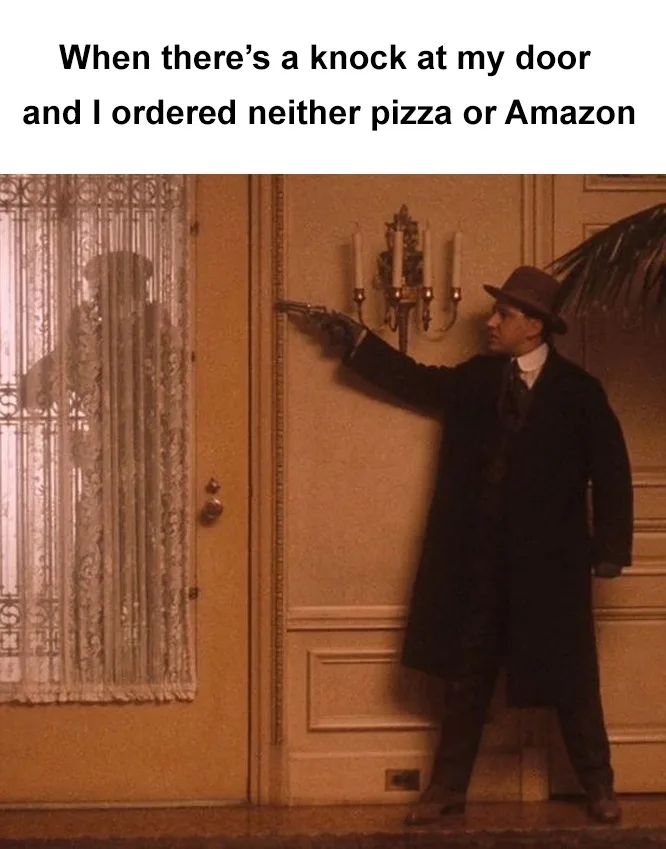 A man in a dark coat and hat stands by an interior door, pointing a revolver at the door handle. His shadow is visible…