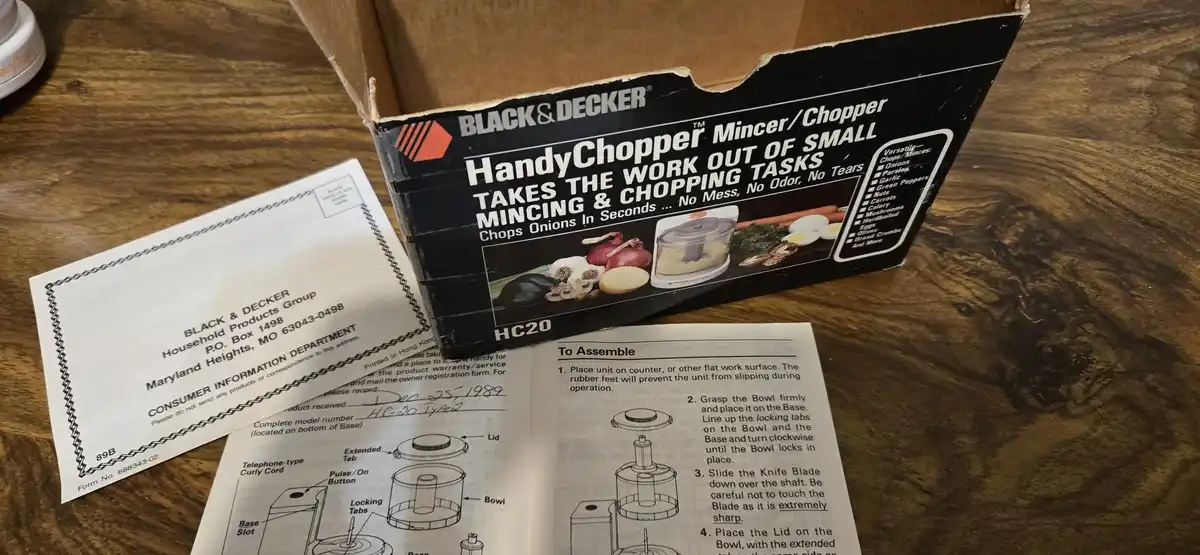 A vintage Black & Decker HandyChopper box, assembly manual, and warranty card are laid out on a wooden table. The box…