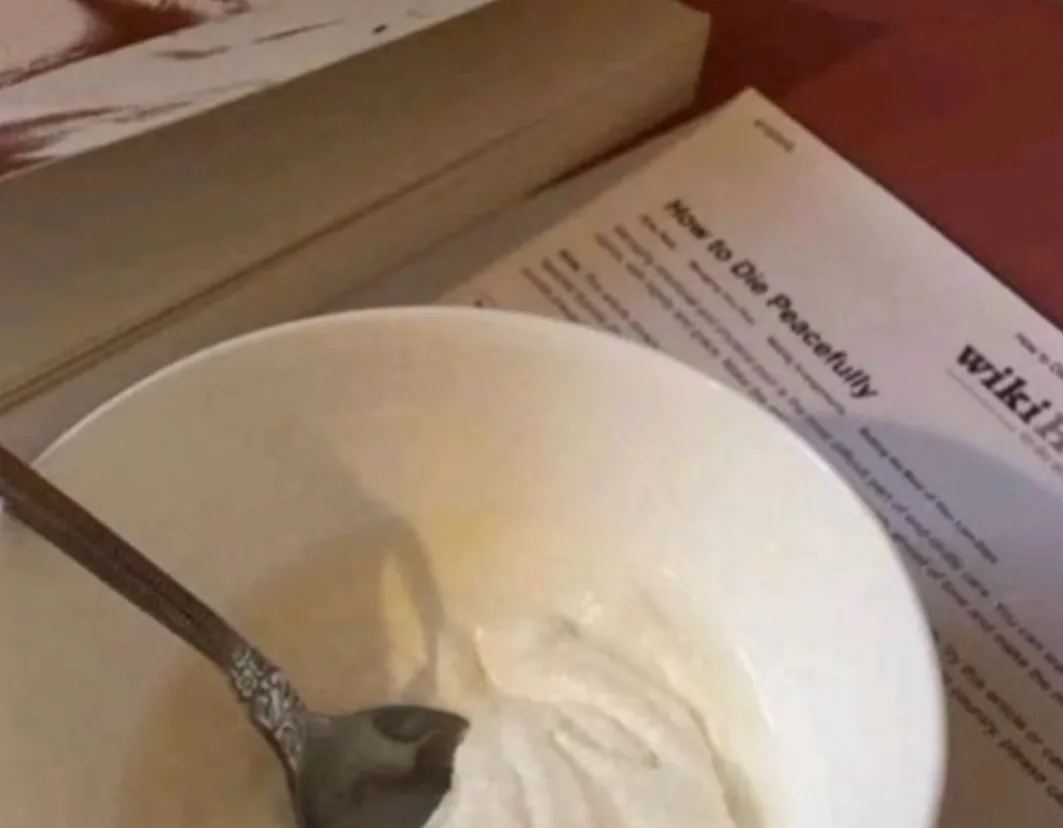 A close-up photo shows a white bowl with a spoon resting inside, containing a creamy white substance, likely yogurt or…