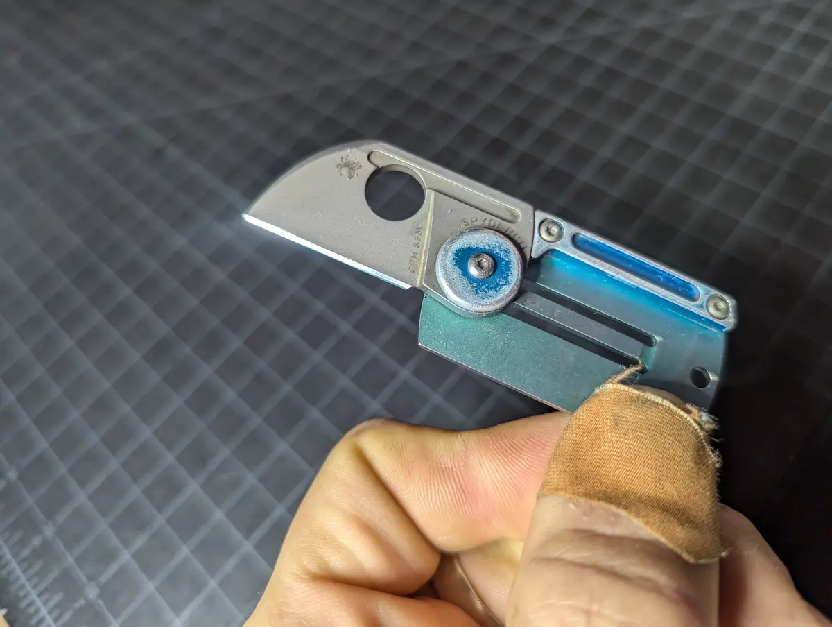 A close-up photo shows a person's hand holding a Spyderco folding knife with a blue and silver handle, the blade partially…
