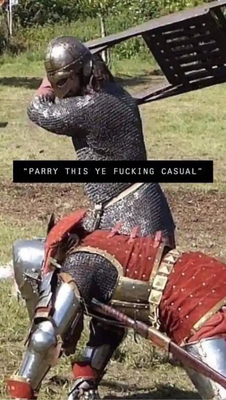 A person in full medieval armor, including chainmail and a helmet, is shown in a defensive stance while holding a large…