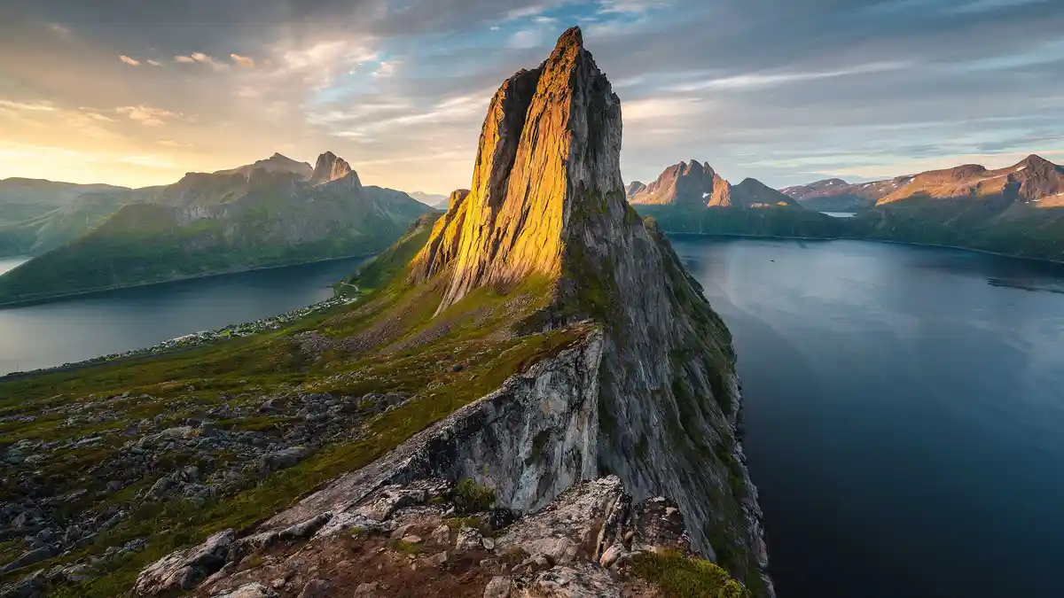 On Senja Island's rugged coastline, the distinctive needle-like spire of Mount Segla rises from the landscape, marking the…