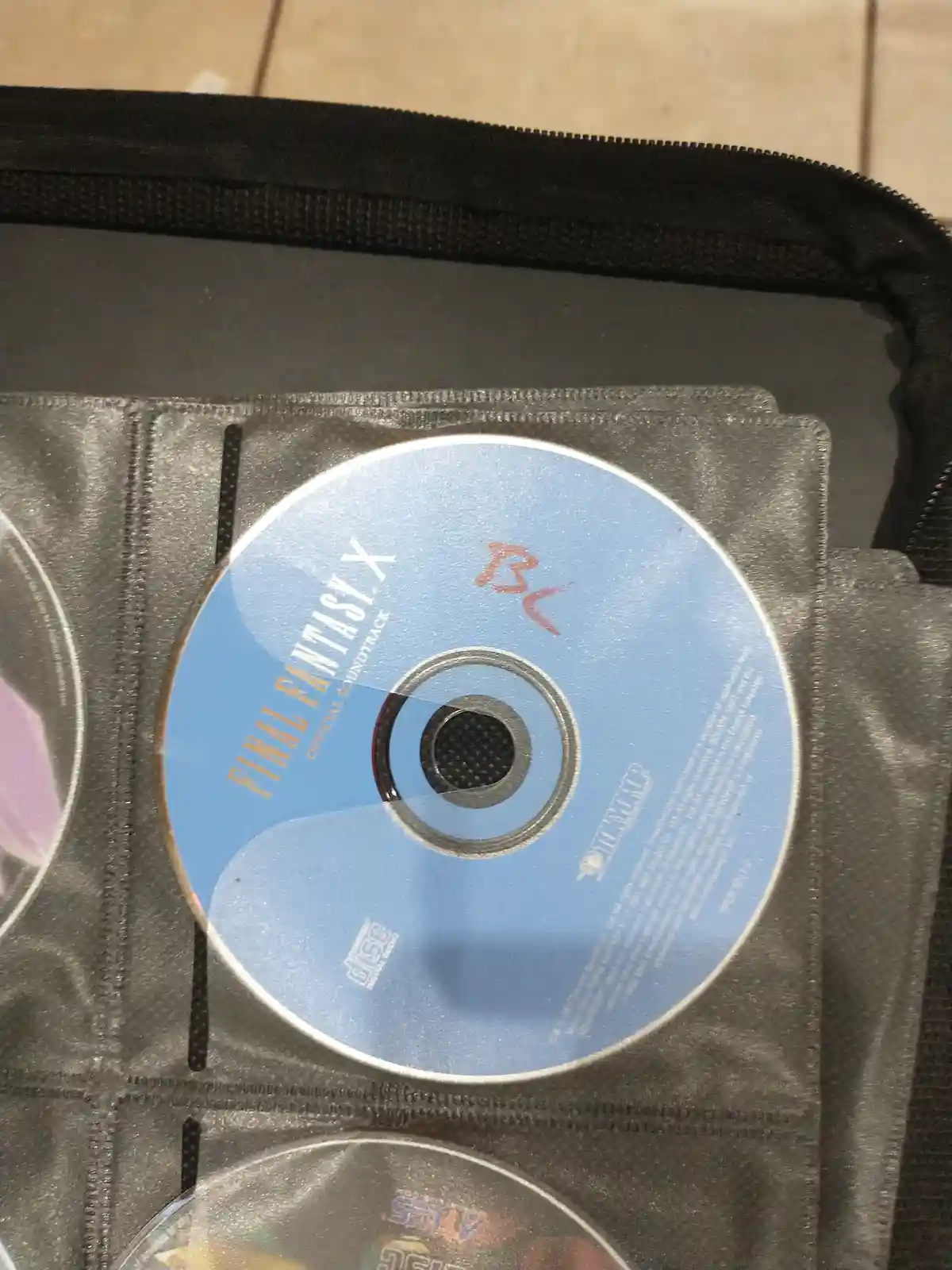 A close-up photo shows a light blue 'Final Fantasy X Official Soundtrack' CD inside a clear plastic sleeve within a black…