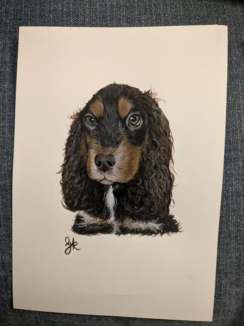A watercolor painting on cream paper depicts a close-up of a puppy with long, wavy dark brown and tan fur, large expressive…