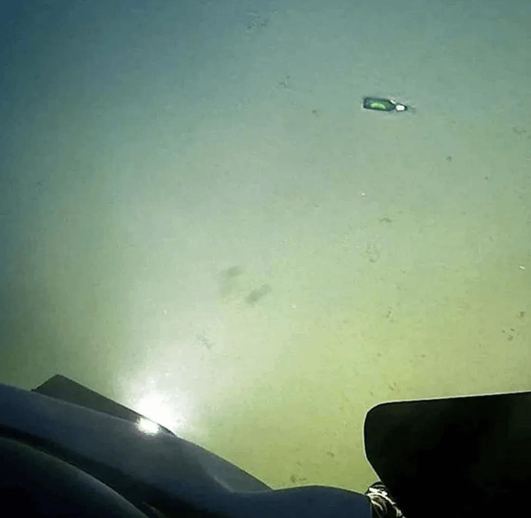 A first-person view from underwater shows a murky, greenish ocean floor with a small, dark bottle floating in the distance…