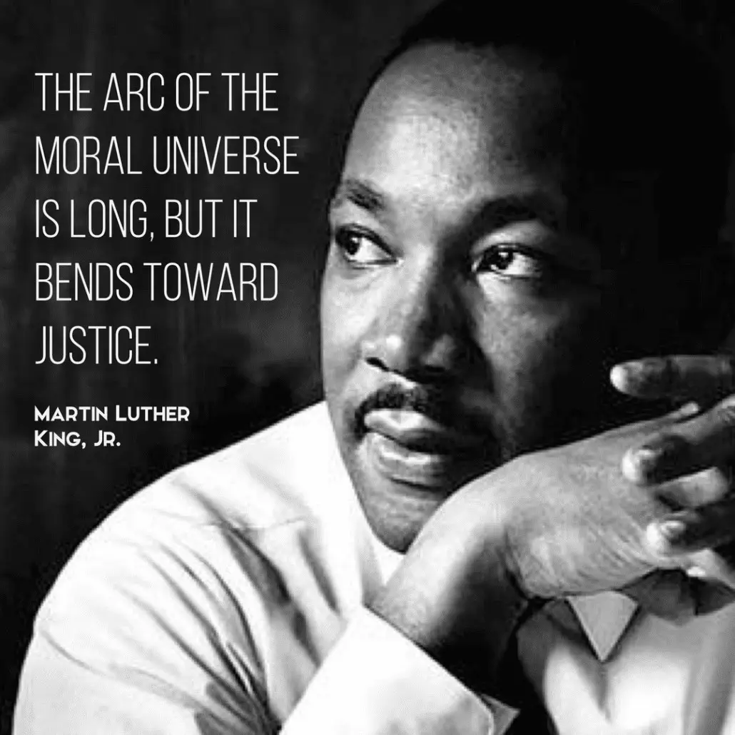 A black and white portrait of Martin Luther King Jr. looking thoughtfully to the side, with his hand resting under his chin…