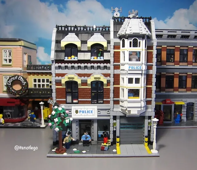 A detailed LEGO model of a police station with 'POLICE' signs on multiple levels, featuring LEGO minifigures including a…