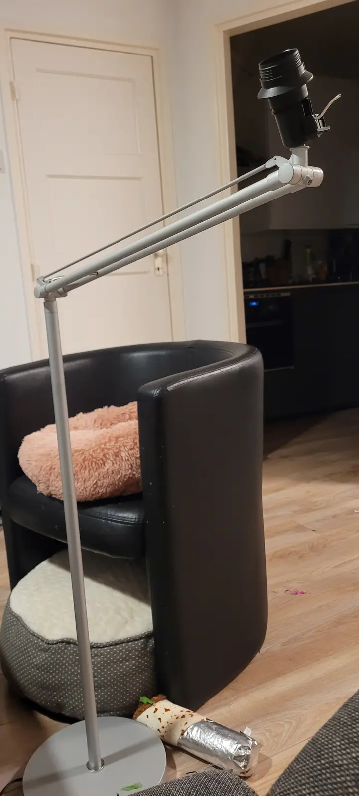 A silver articulated desk lamp with a black light bulb socket is positioned over a black leather chair with a pink fluffy…