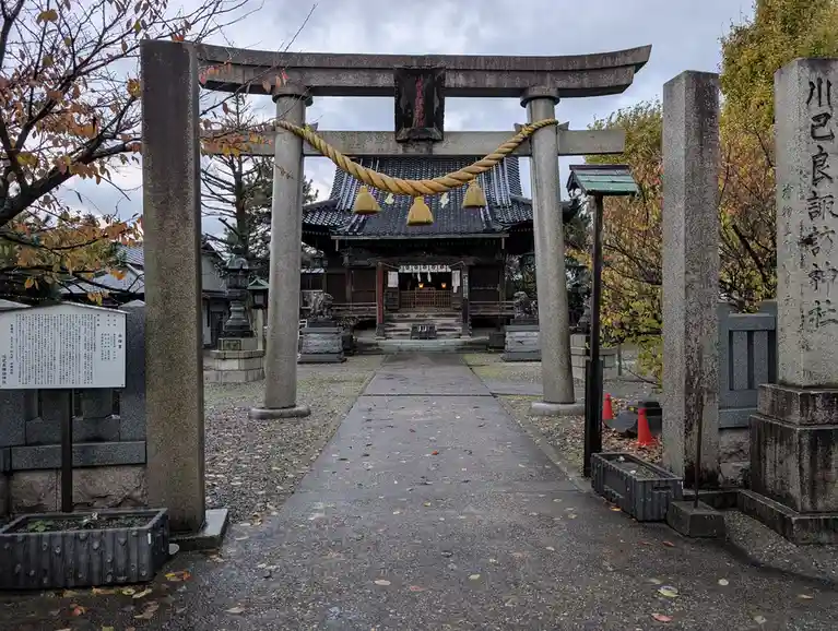 A photo of a traditional Japanese shrine entrance featuring a large stone torii gate with a thick rope and tassels, leading…