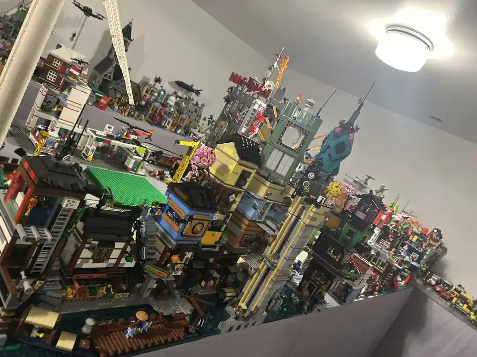 A sprawling, tilted LEGO cityscape featuring numerous detailed buildings, vehicles, and minifigures, with a red sign reading…