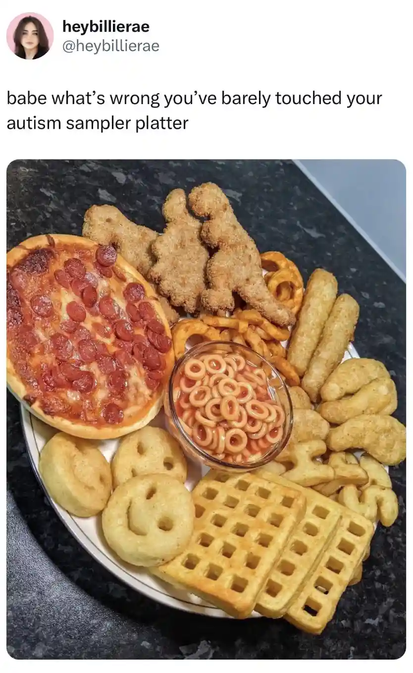 A plate overflowing with various kid-friendly, processed foods including a small pepperoni pizza, dinosaur-shaped chicken…