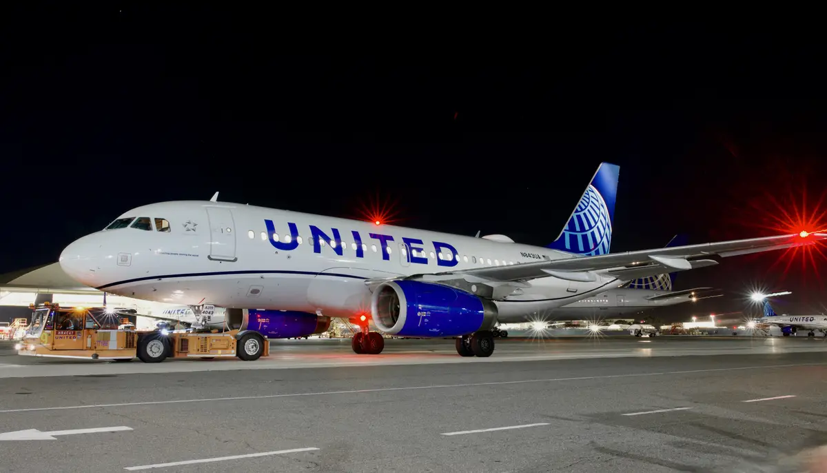A United Airlines passenger jet is parked at night on an airport tarmac, illuminated by red navigation lights and ground…