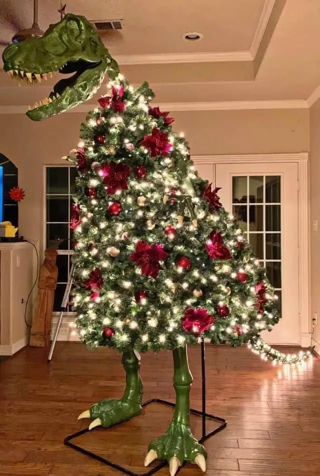 a christmas tree decorated with white lights and red ornaments is mounted on a green t-rex dinosaur statue, which has its…