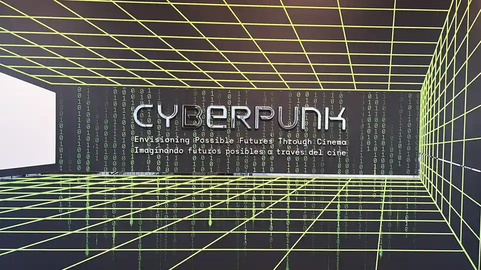 A futuristic room with neon yellow grid lines on walls and floor, featuring a large metallic 'CYBERPUNK' sign. Behind it, a…