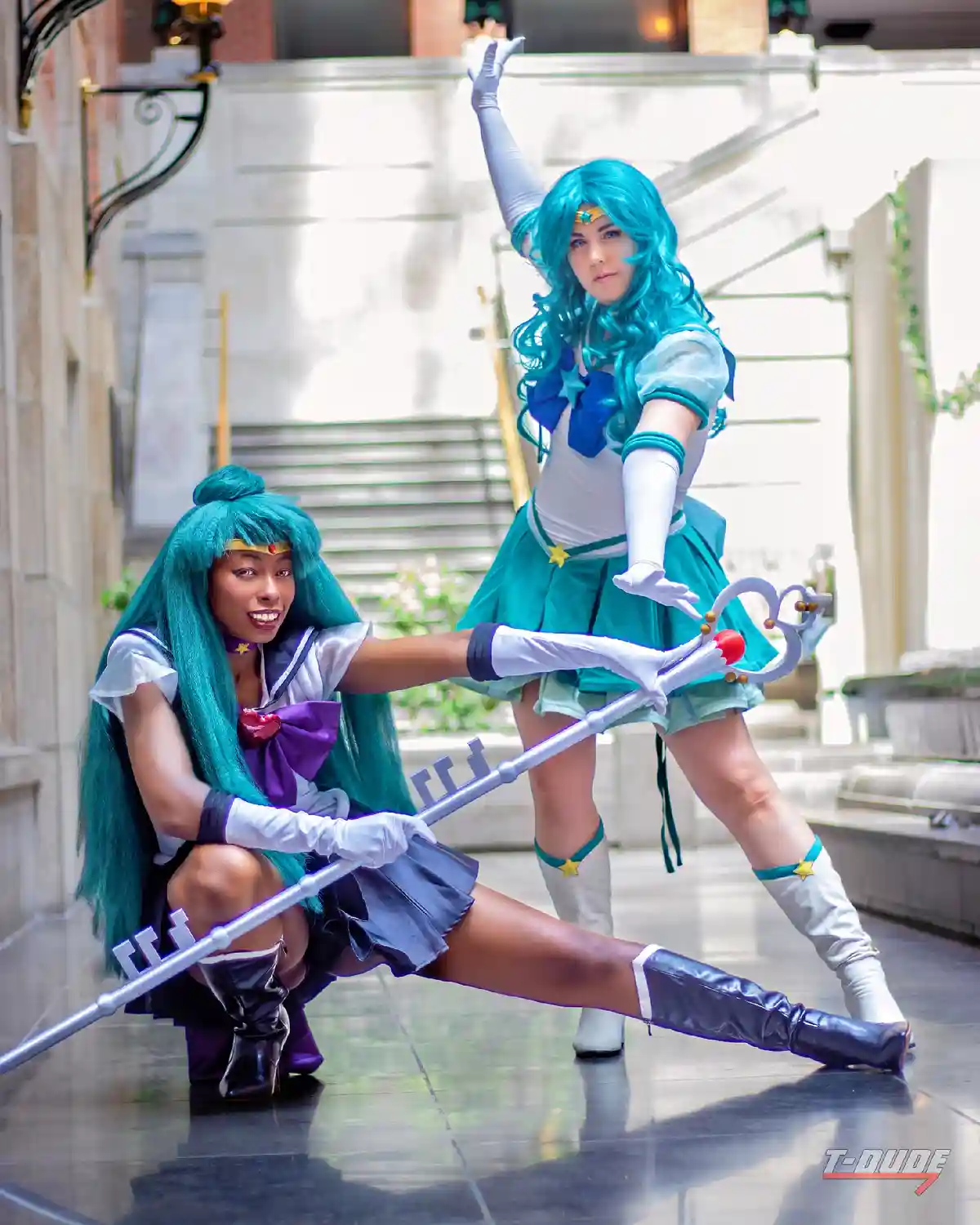 Two cosplayers dressed as Sailor Uranus and Sailor Neptune from Sailor Moon pose dynamically in a public building, holding a…