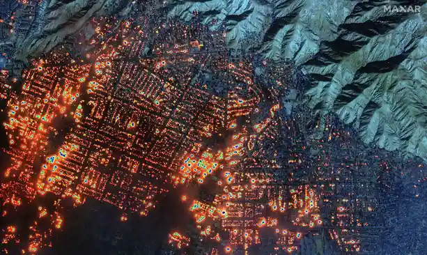 a satellite night view of a sprawling city nestled between rugged mountains, illuminated by thousands of bright orange and…