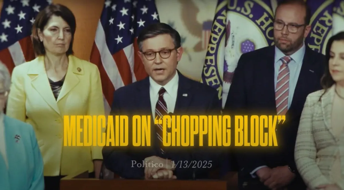A still image from a 2025 Politico news report shows a man in a suit speaking at a podium with American flags and U.S. House…