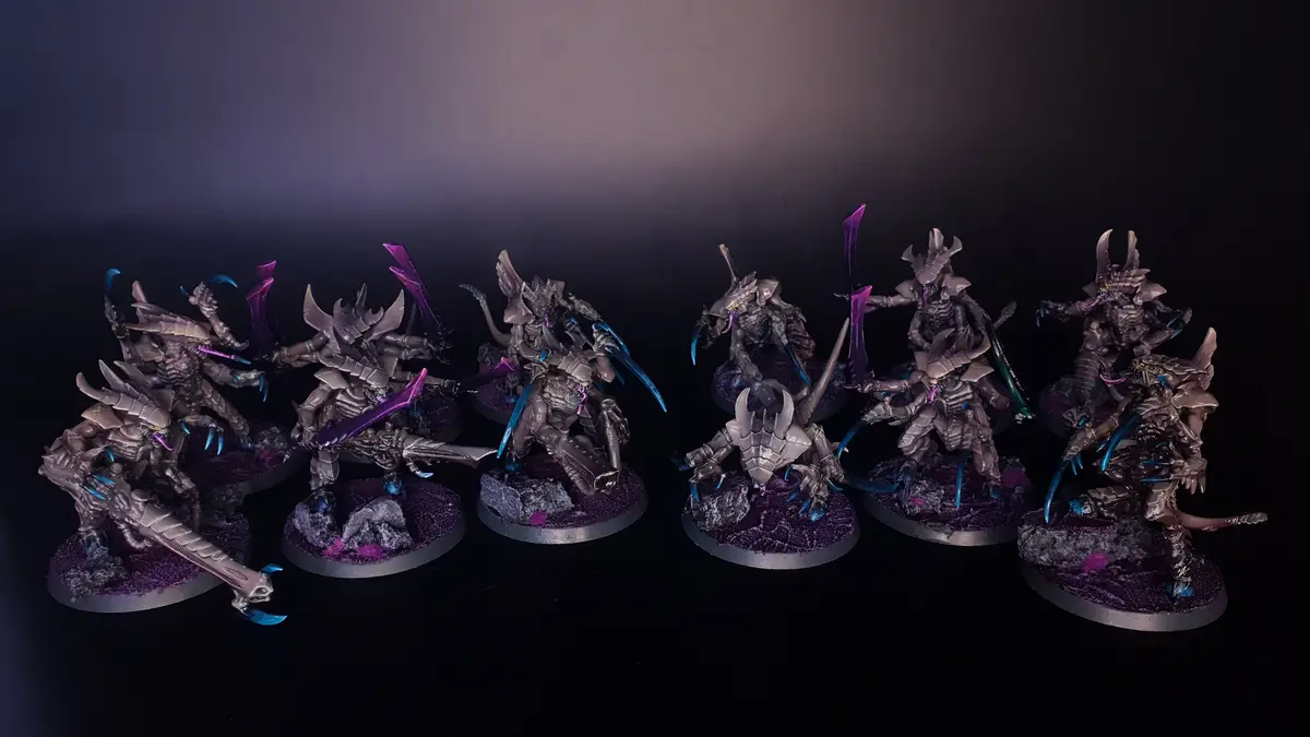 A row of intricately painted fantasy miniatures, resembling armored insectoid warriors with purple and blue accents, are…