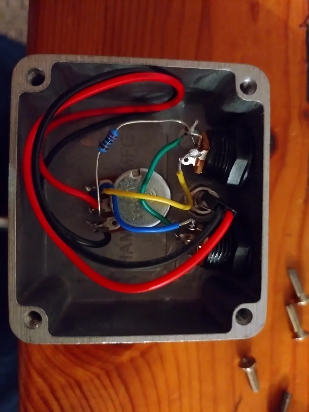 A top-down view of a metal electrical enclosure with colorful wires (red, black, green, yellow, blue) connected to a small…