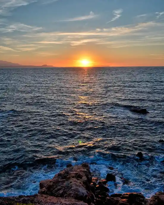 A serene sunset over the ocean with the sun low on the horizon, casting golden reflections on the water, and waves crashing…