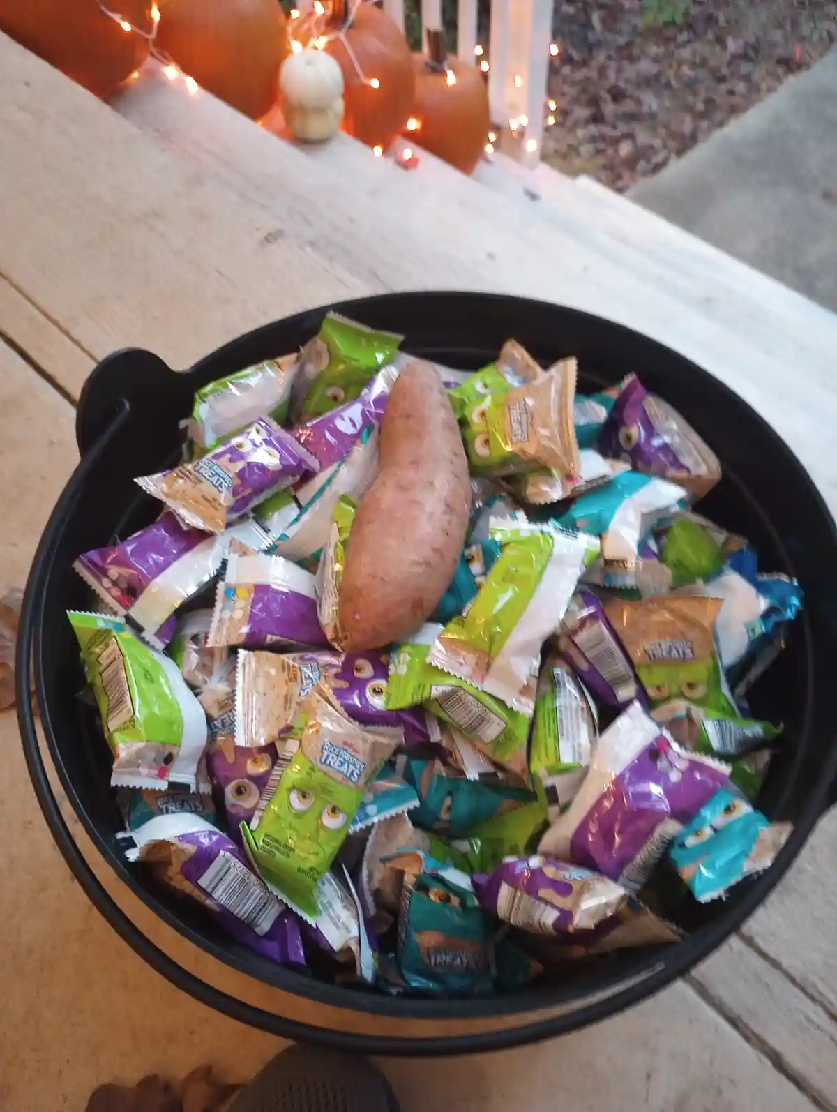 A black cauldron-style bucket filled with Halloween candy, mostly Rice Krispies Treats in green, purple, and teal wrappers…