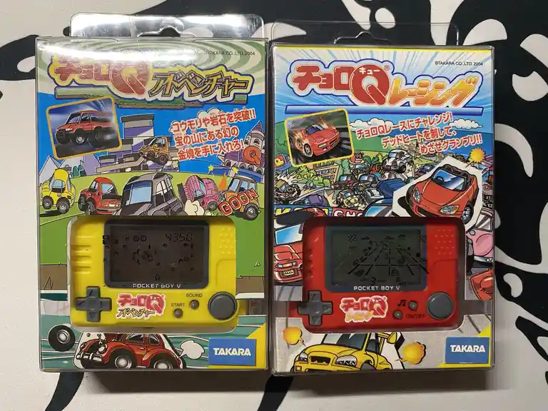 Two Takara Pocket Boy V handheld game devices in their original packaging, one yellow labeled 'cho-q adventure' showing a…