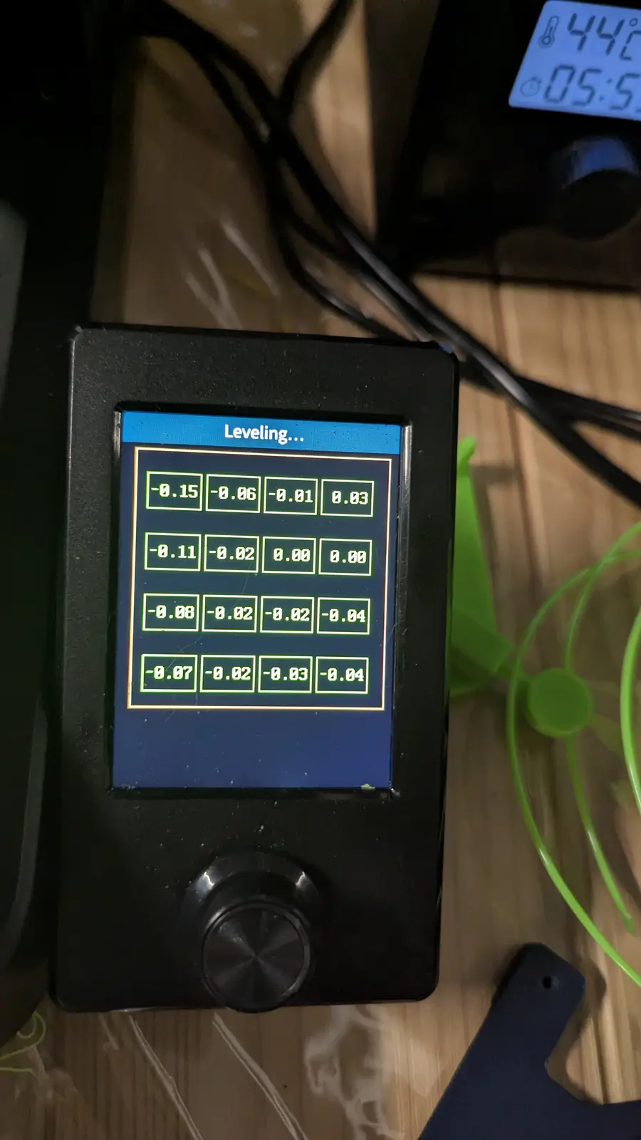 A close-up of a black 3D printer bed leveling controller displaying a grid of small decimal numbers like -0.15, -0.06, 0.00…