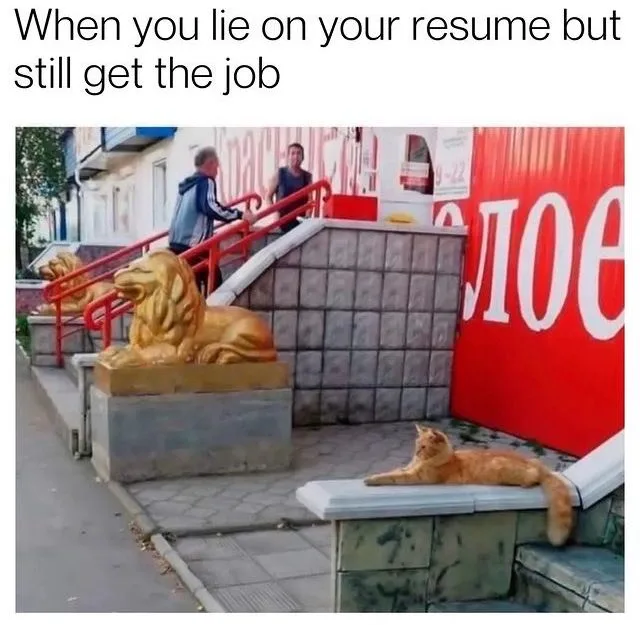 A real cat lounges lazily on a low stone ledge in front of a building entrance, while two men stand on a set of stairs…