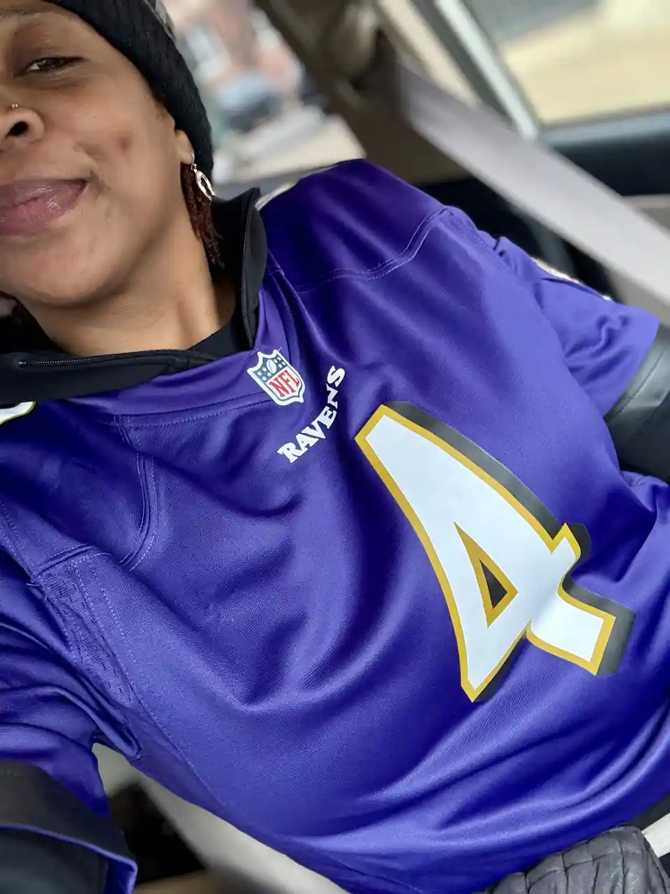 A person wearing a purple Baltimore Ravens NFL jersey with the number 4 prominently displayed on the chest. The jersey…