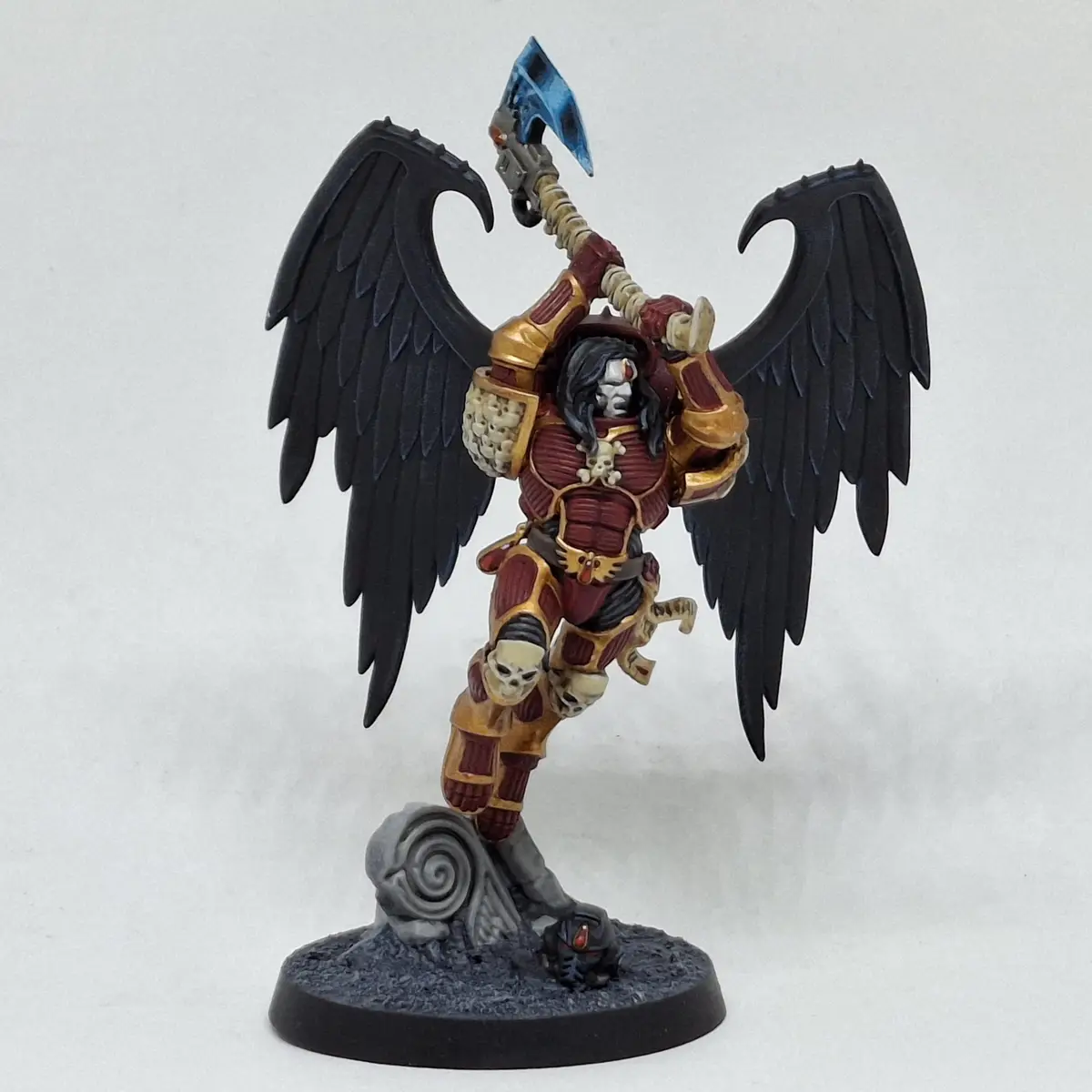 A painted miniature of a winged, armored warrior with black wings, holding a large blue axe, standing on a base with a snail…