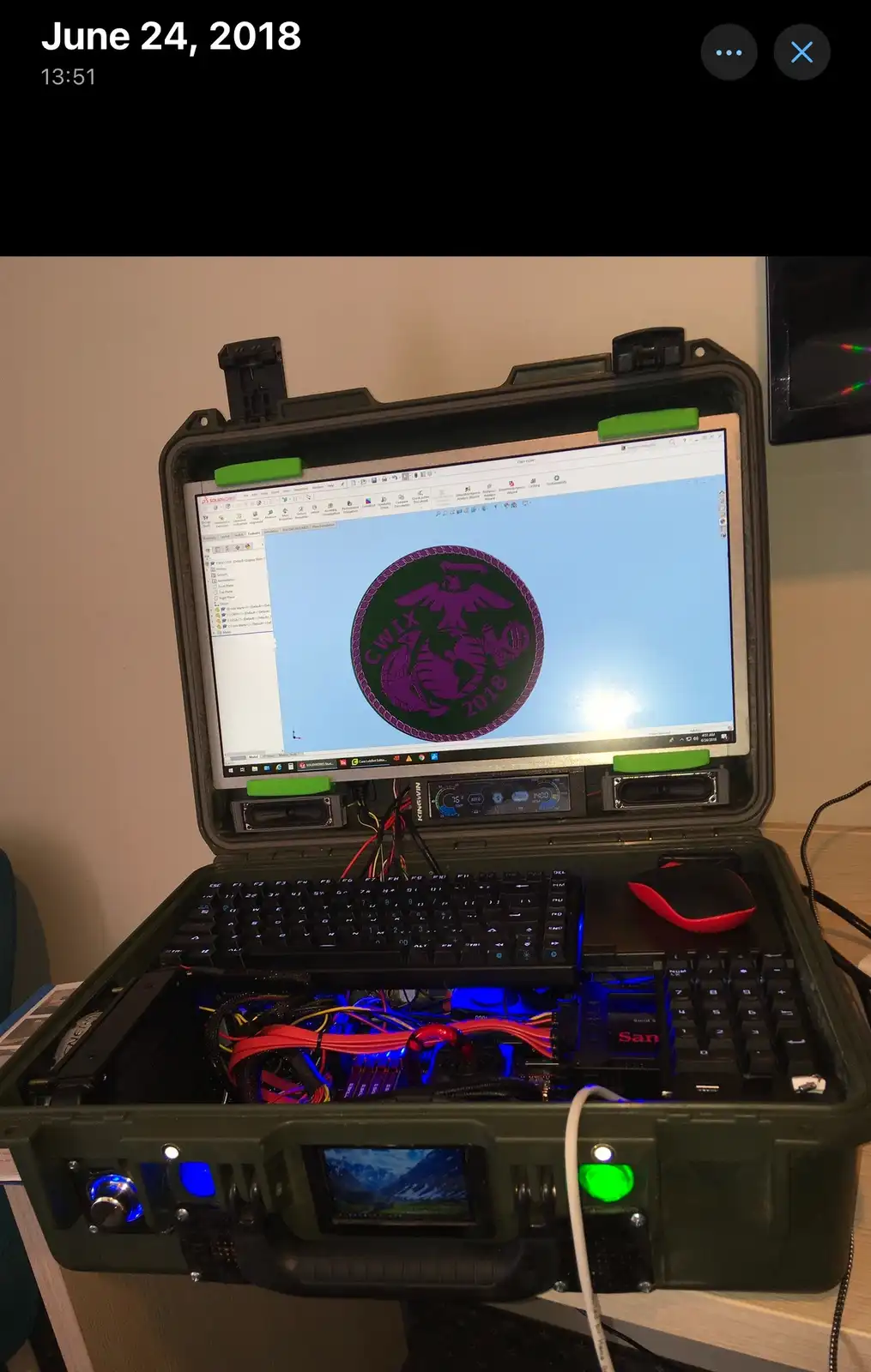 A custom-built computer housed inside a rugged green military-style case, with a monitor displaying a purple and green…