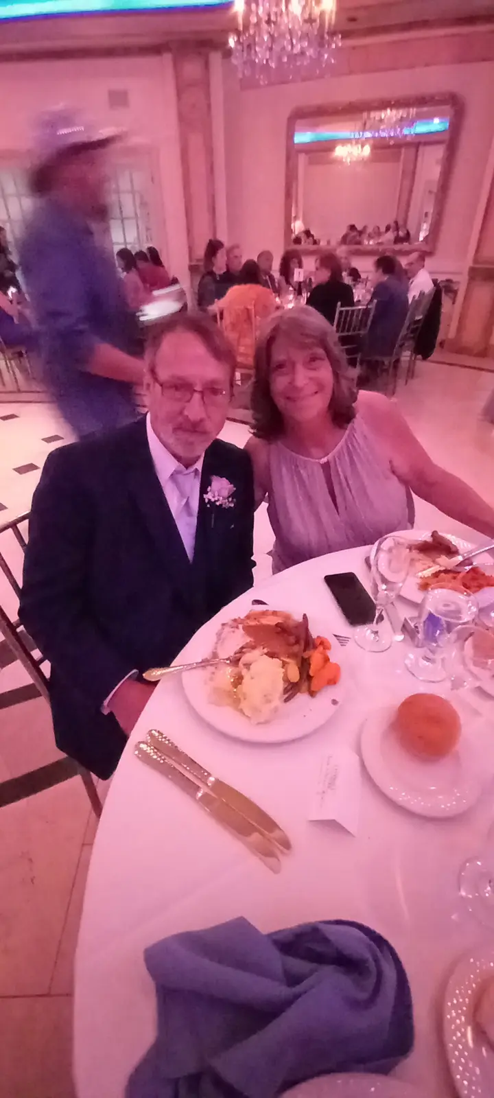 A blurry photo of a man and woman sitting at a formal dinner table with partially eaten food, a waiter blurred in motion…