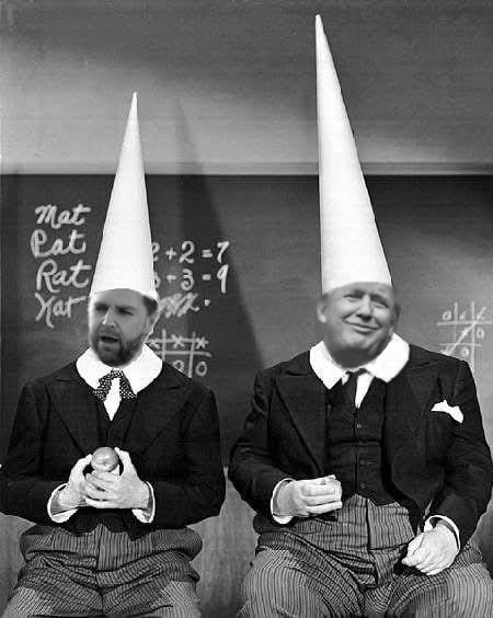 Two men in suits and tall white pointed hats sit in front of a chalkboard with math equations and the words 'Mat Cat Rat…