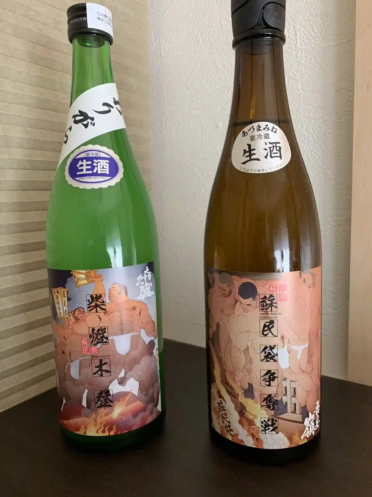 Two bottles of Japanese sake sit side by side on a dark wooden surface, one green and one brown, both featuring explicit…