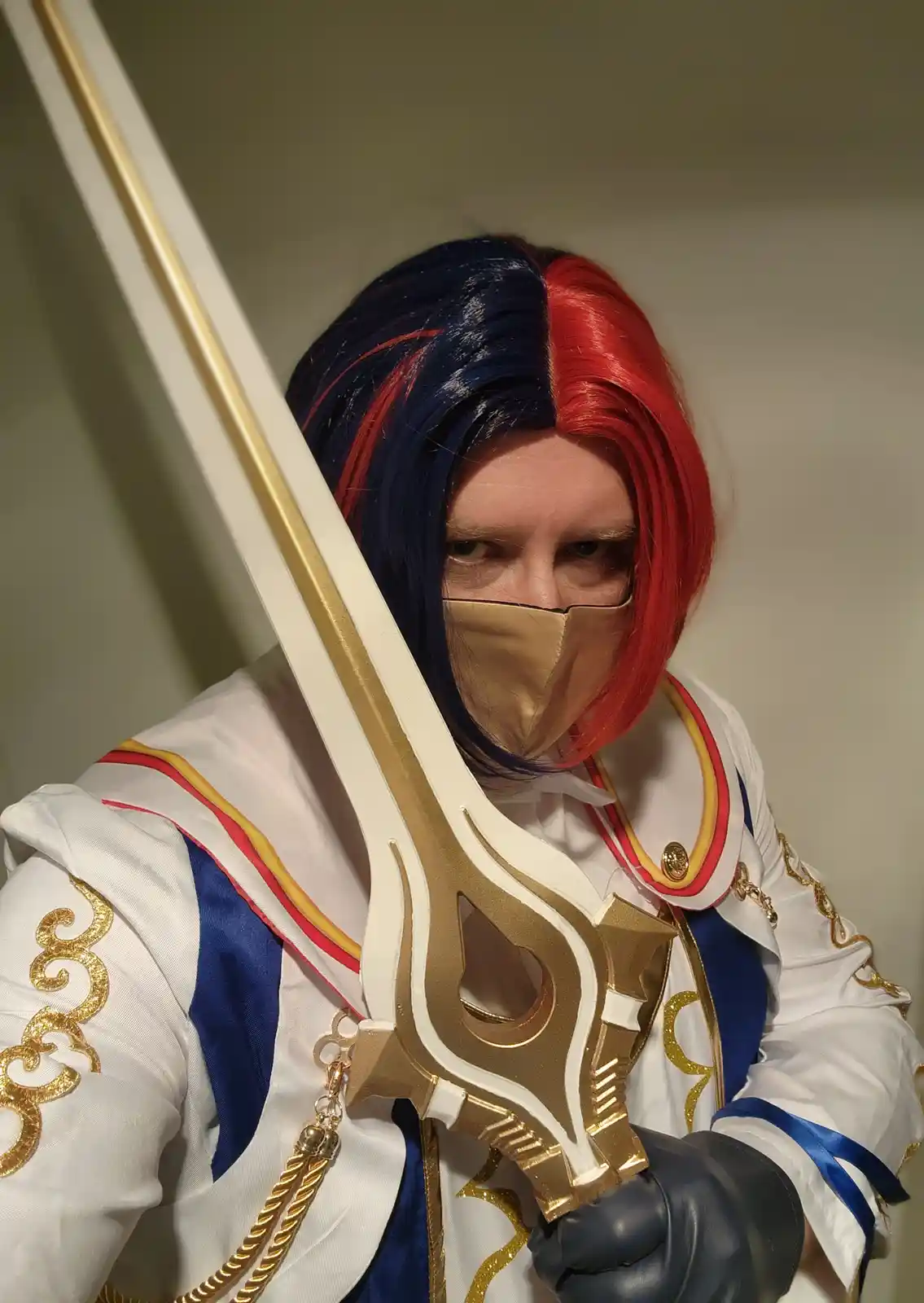 A person in a detailed cosplay of a character with a blue and red half-and-half wig, wearing a gold face mask and holding a…