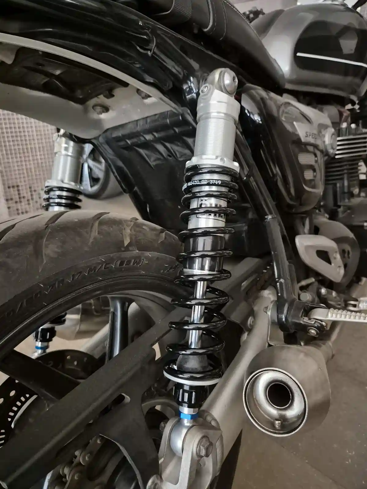 A close-up photo of a motorcycle's rear suspension, showing a silver shock absorber with black coil springs mounted between…