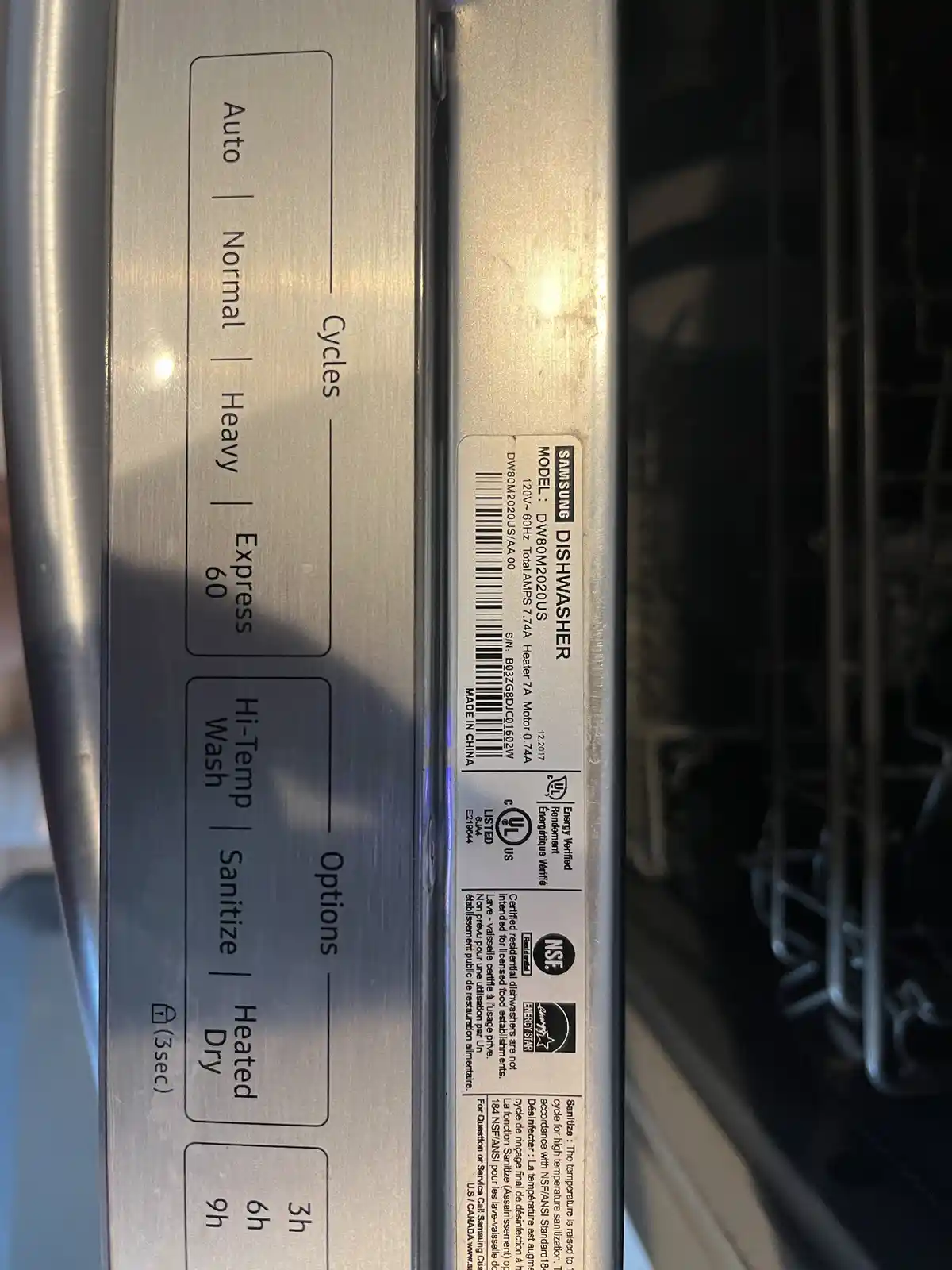 A close-up photo of a Samsung dishwasher's control panel and model label, showing cycle options like 'Auto', 'Normal'…