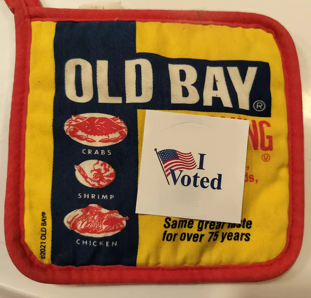 A yellow and red Old Bay seasoning pot holder with images of crabs, shrimp, and chicken, has a white 'I Voted' sticker with…