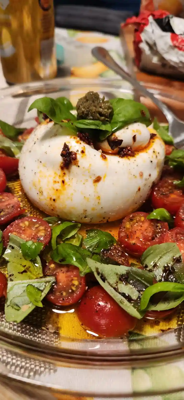 A close-up photo of a caprese salad featuring a large ball of fresh mozzarella cheese, halved cherry tomatoes, and basil…