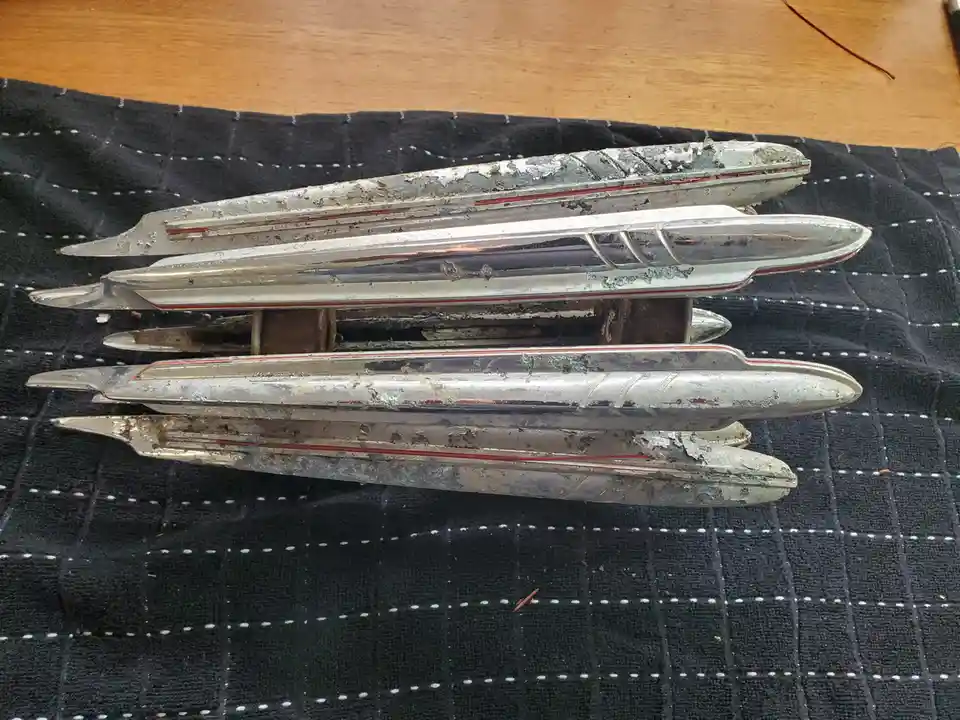 A close-up photo shows four weathered, silver-colored, elongated toy boats or model submarines with peeling paint and red…