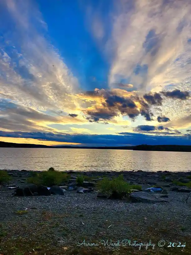 A scenic photograph of a lake at sunset or sunrise, with vibrant blue and golden clouds streaking across the sky above calm…