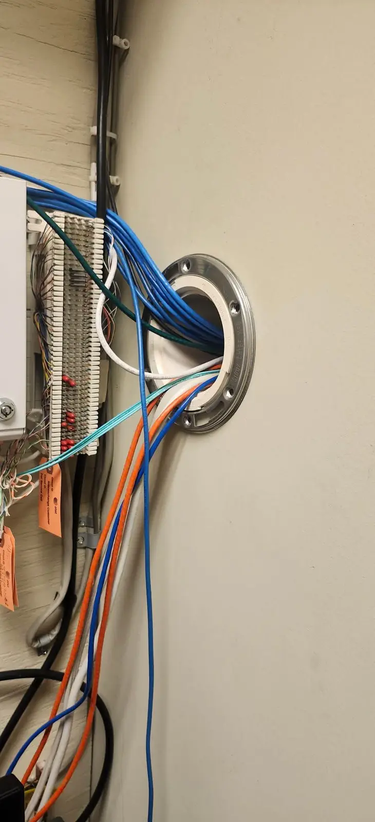 A close-up photo shows a wall-mounted electrical panel with numerous colorful wires (blue, orange, white, black, green)…