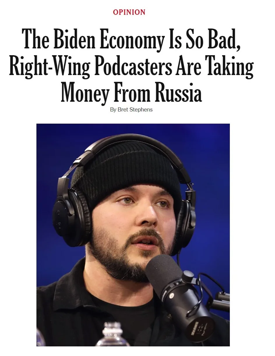 The image shows a man with a beard wearing a black beanie and large headphones, speaking into a microphone against a blue…