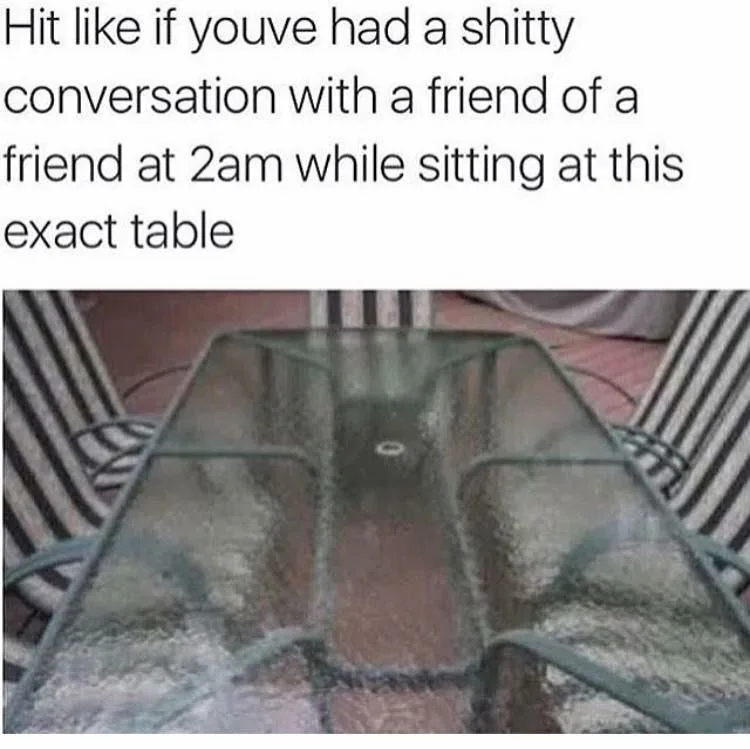 The image shows a close-up, slightly blurry view of a glass-top outdoor table with metal legs and striped chairs around it…