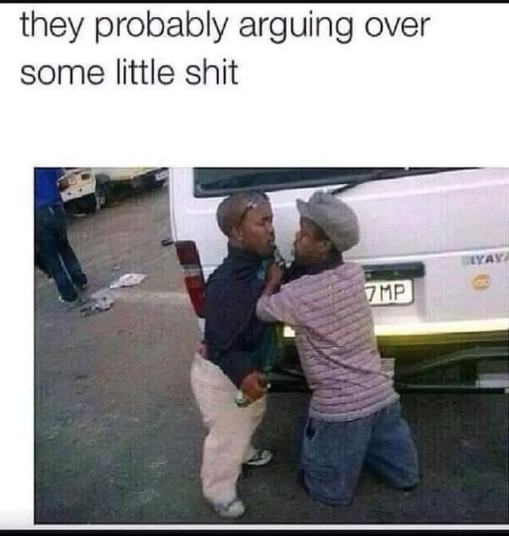 Two men are physically confronting each other in front of a white van, one standing and one kneeling, appearing to be in a…