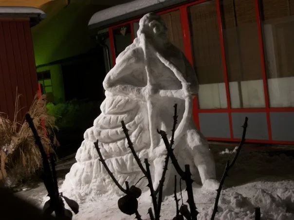 A large, detailed snow sculpture of a seated figure with a long beard and draped clothing, resembling a historical or…