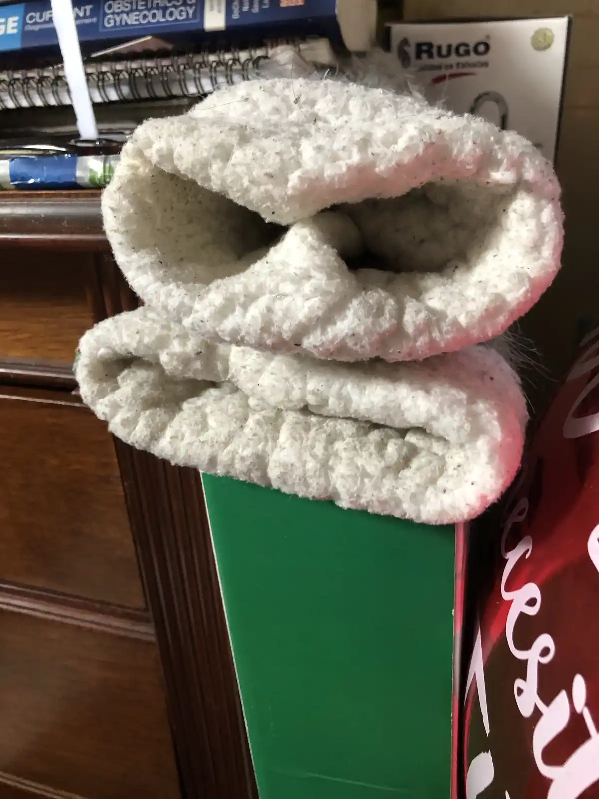 A crumpled, white, fuzzy sock with pink trim is draped over the top of a green and red soda can, resembling a face with a…
